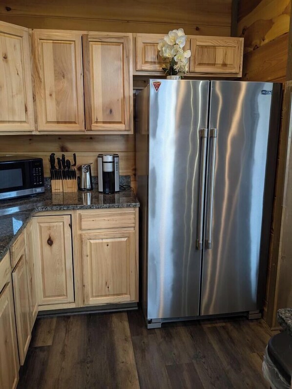 A kitchen with wooden cabinets, a stainless steel refrigerator, a microwave, and a coffee maker. - High Point Ridge (Sevierville)