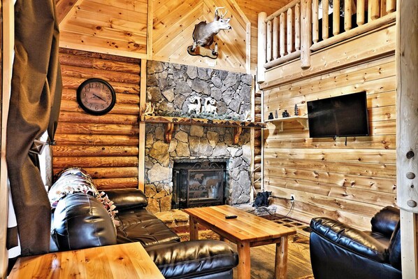 Ein Blockhaus-Interieur mit Kamin aus Stein, Ledersitzmöbeln, einem Holztisch und einem aufgehängten Hirschkopf.