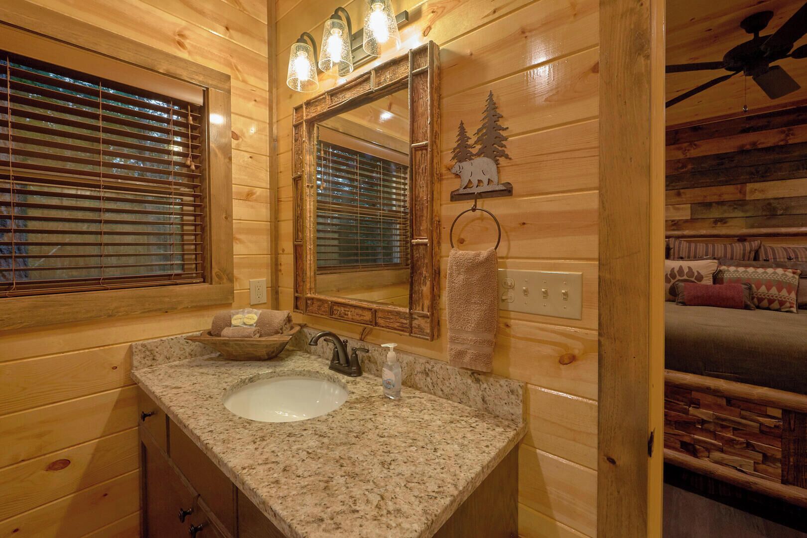 A wooden cabin bathroom with a granite sink, a mirror, a towel ring, and a window with blinds.