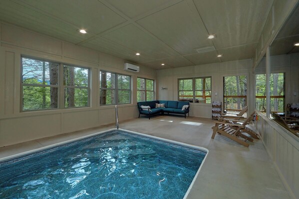 Une grande piscine intérieure avec un sol carrelé de bleu, un canapé bleu et des chaises longues en bois.