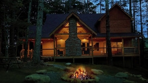 A log cabin with a stone fireplace, wooden deck, and a fire pit in the yard. - Adventure Lodge (Sevierville)