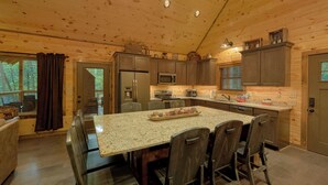 A wooden cabin-style kitchen with granite countertops, dark wooden chairs, and a central island. - Adventure Lodge (Sevierville)