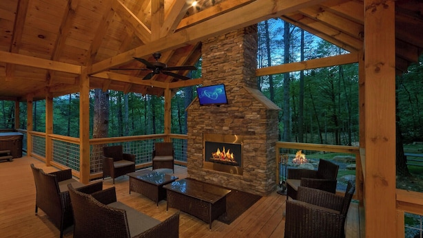 A wooden deck with wicker furniture, a stone fireplace, and a TV mounted on the wall. - Adventure Lodge (Sevierville)