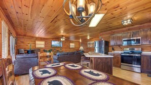 Interior acogedor de una cabaña con una mesa de comedor de madera, un sofá y una zona de cocina con electrodomésticos modernos.