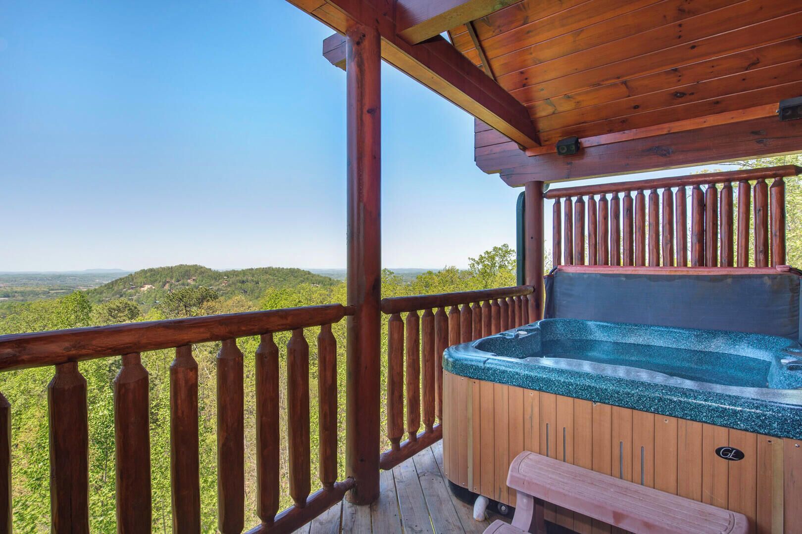 A wooden deck with a hot tub and a bench, overlooking a forested landscape.