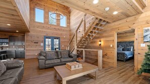A cozy log cabin interior with a living room, sofa, coffee table, staircase, and a bedroom. - The Phoenix (Sevierville)