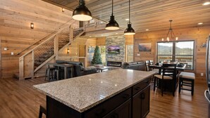A spacious kitchen with a granite island, wooden walls, and a stone fireplace. - The Phoenix (Sevierville)