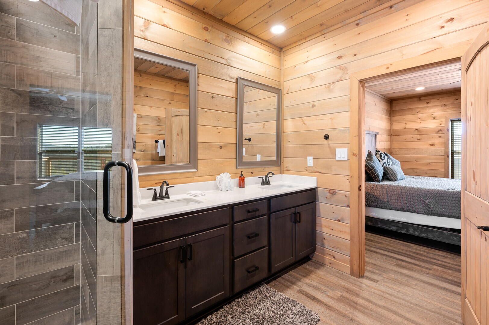 A modern bathroom with a wooden interior, a glass shower enclosure, and a bed with a view.