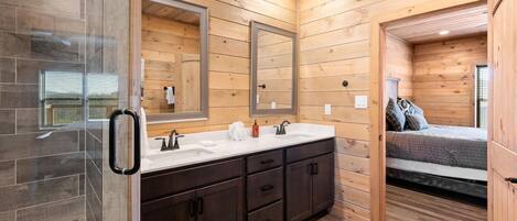 A modern bathroom with a wooden interior, a glass shower enclosure, and a bed with a view.