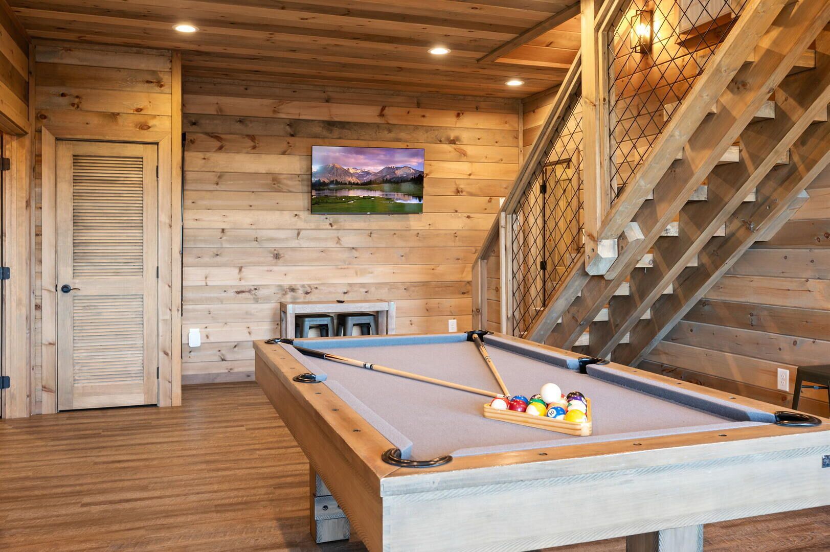 A pool table in a wooden room with a staircase and a painting on the wall.