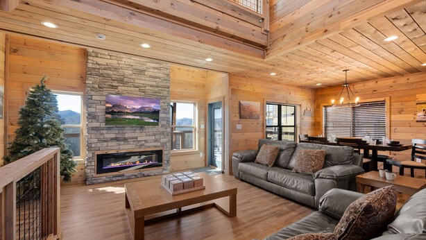 A cozy cabin interior with a stone fireplace, leather sofa, wooden floors, and a dining area. - The Phoenix (Sevierville)