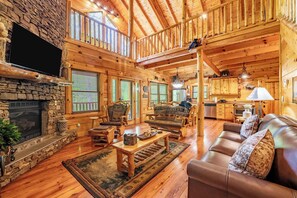 A spacious log cabin with a stone fireplace, wooden furniture, and a kitchen area. - Smoky Bear Cabin (Sevierville)