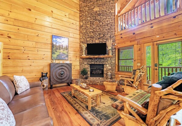 Un interior de cabaña acogedor, con chimenea de piedra, paredes de madera, sofá de cuero y decoración rústica.