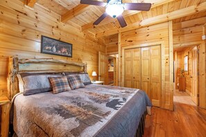Un dormitorio de cabaña de madera con una cama, un ventilador de techo y una puerta que da a otra habitación.