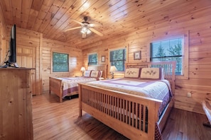 Une cabane avec deux lits en bois, un ventilateur de plafond et de grandes fenêtres.