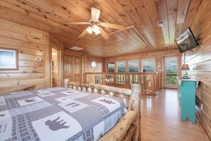 A wooden cabin interior with a bed, ceiling fan, and large windows offering a view. - Starr Crest Lodge (Sevierville)