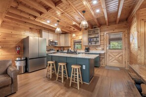 A wooden cabin interior with a kitchen, bar stools, and a fire extinguisher. - Starr Crest Lodge (Sevierville)