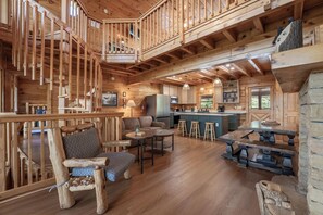A spacious wooden cabin interior with a central dining area, kitchen, and a loft bedroom with a balcony. - Starr Crest Lodge (Sevierville)
