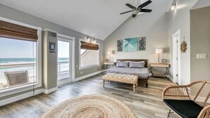A bedroom with a bed, bedside tables, a chair, a view of the beach, and a ceiling fan. - Green Reef #6- Beachfront Bliss (Destin)