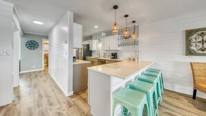 A modern kitchen with white cabinets, a central island, and bar stools. - Green Reef #6- Beachfront Bliss (Destin)