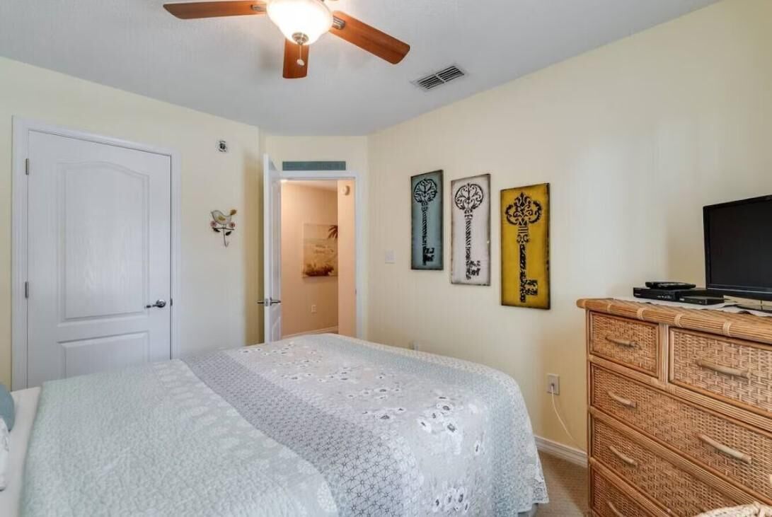 Un dormitorio con cama, ventilador de techo, cómoda y decoración en la pared.