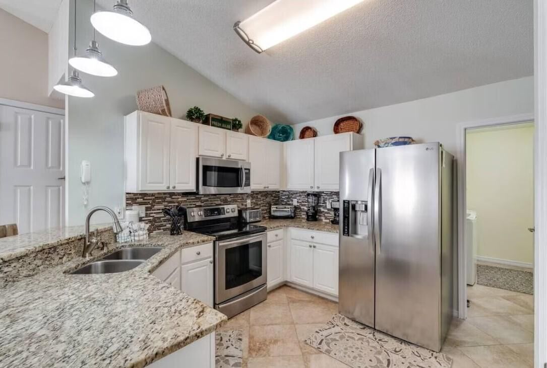 A modern kitchen with white cabinets, stainless steel appliances, granite countertops, and a patterned backsplash.