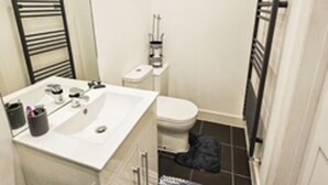 A small bathroom with a white sink, a mirror, a toilet, and a black towel rack. - Orpington Cozy Retreat With 3 Bed (Orpington)