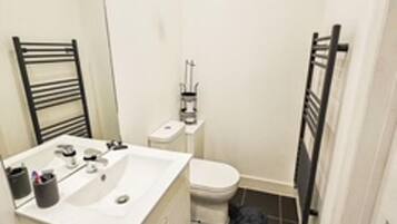 A small bathroom with a white sink, a mirror, a toilet, and a black towel rack.