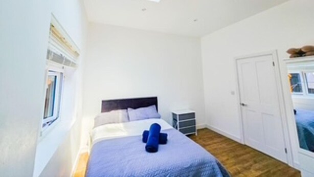 A bedroom with a skylight, a bed with a blue blanket, a small bedside table, and a wardrobe. - Orpington Cozy Retreat With 3 Bed (Orpington)