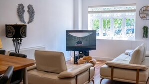 A living room with a sofa, a television, and a window with a view of greenery. - Orpington Cozy Retreat With 3 Bed (Orpington)