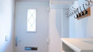 A room with a white door, a small window with a diamond pattern, a coat rack with a wooden hanger, and a white shelf. - Orpington Cozy Retreat With 3 Bed (Orpington)