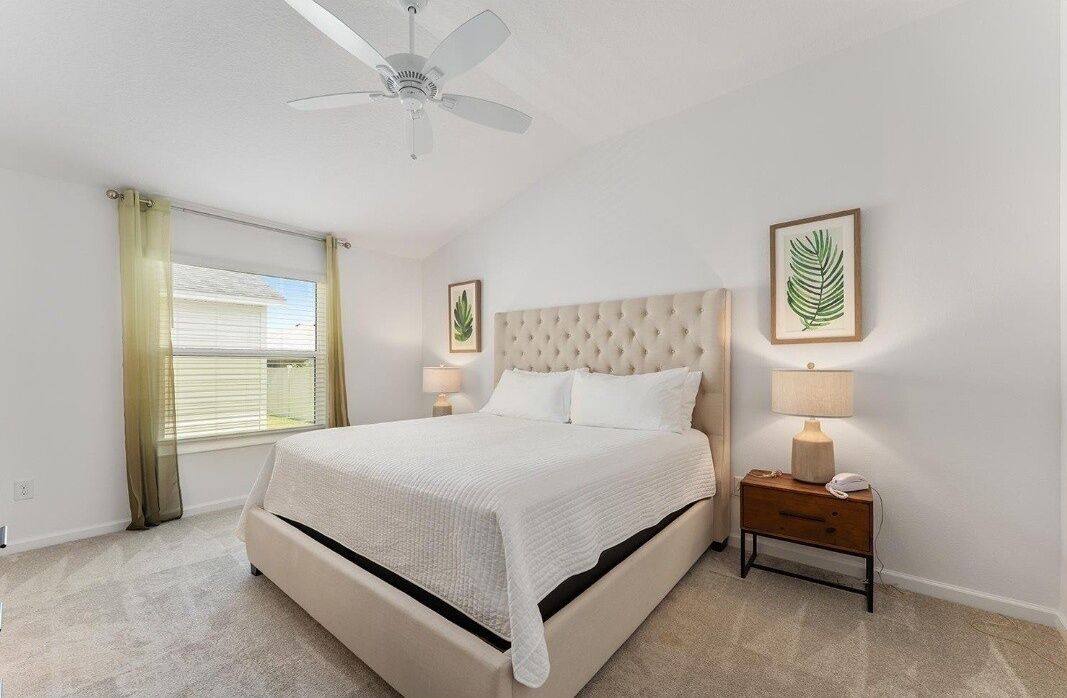 A bedroom with a bed, a ceiling fan, a nightstand with a lamp, and framed leaf artwork on the wall.