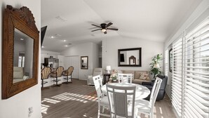 A spacious living area with a dining table, chairs, and a ceiling fan. There is a large window with blinds, a sofa, and a plant. - Stylish Golfside Getaway (Wildwood)