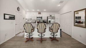 A modern kitchen with white cabinets, a central island, and three upholstered chairs. - Stylish Golfside Getaway (Wildwood)