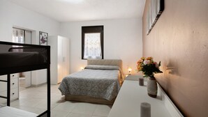 Un dormitorio con cama, mesita de noche, lámpara y ventana.