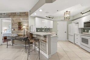 A modern kitchen with white cabinets, a central island, and a dining area with a table and chairs.