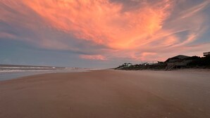 A beach with a sunset, sandy shore, and houses in the background. - Most complete resort like in New Smyrna Beach (New Smyrna Beach)