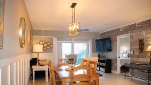 A dining area with a wooden table and chairs, a chandelier, and a television in the background. - Most complete resort like in New Smyrna Beach (New Smyrna Beach)