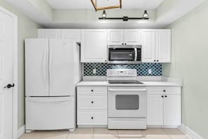 A kitchen with white cabinetry, a refrigerator, a microwave, an oven, and a tiled backsplash.