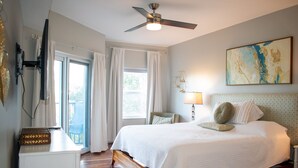 A bedroom with a bed, a ceiling fan, a window with curtains, a painting on the wall, and a bedside table. - Most complete resort like in New Smyrna Beach (New Smyrna Beach)