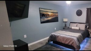 A bedroom with a bed, a clock, a painting, and a TV on the wall. - Private getaway by the beach (Pensacola)
