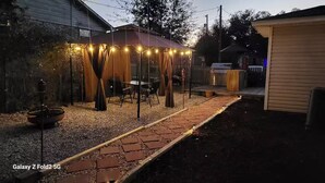A backyard with a covered patio area, a grill, and a garden path. - Private getaway by the beach (Pensacola)