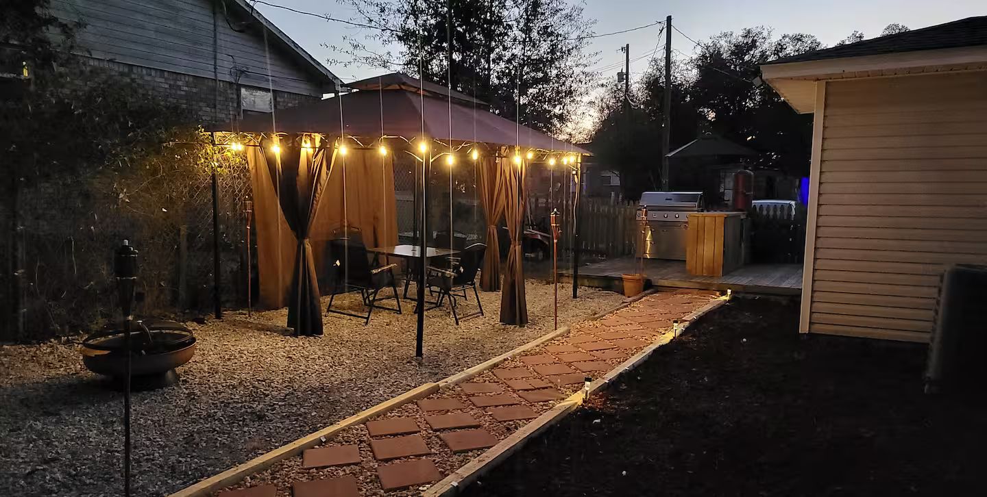 A backyard with a covered patio area, a grill, and a garden path.