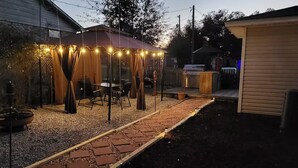 Un cortile con un portico coperto, un barbecue e un vialetto fiorito.