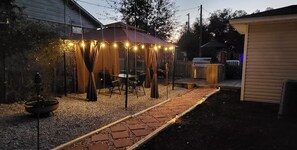 A backyard with a covered patio area, a grill, and a garden path. - Private getaway by the beach (Pensacola)