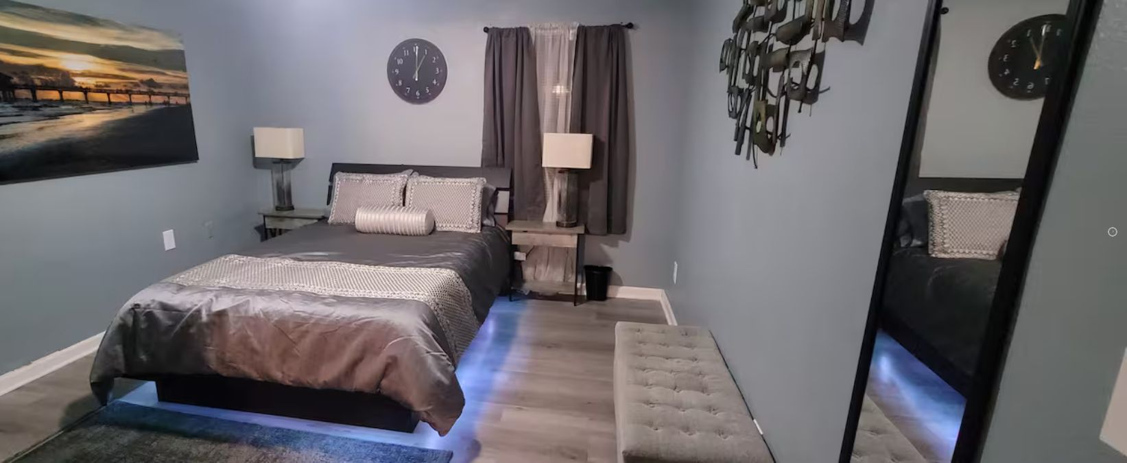 Een slaapkamer met een bed, nachtkastjes, een klok en een schilderij aan de muur.