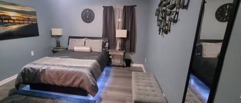 Een slaapkamer met een bed, nachtkastjes, een klok en een schilderij aan de muur.