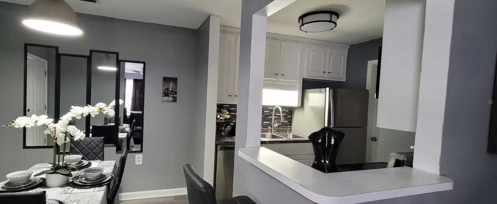 A modern dining area with a Galaxy Z Fold2 50L table, white walls, and a kitchen with white cabinets and stainless steel appliances.