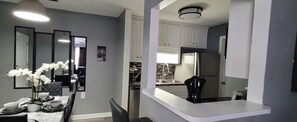 Un espace de salle à manger moderne avec une table Galaxy Z Fold2 50L, des murs blancs et une cuisine dotée de meubles blancs et d’appareils électroménagers en acier inoxydable.