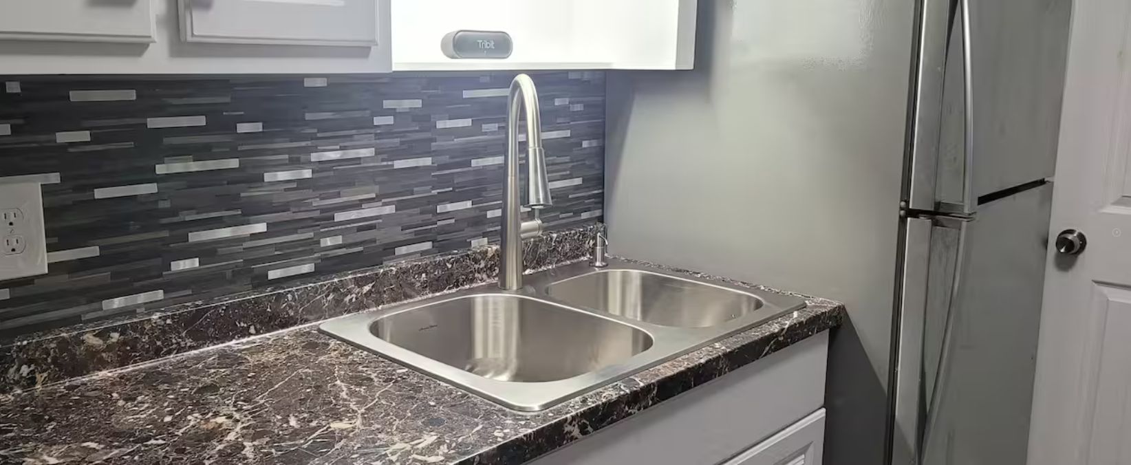 A kitchen with a double sink, a stainless steel faucet, and a backsplash with a geometric pattern.